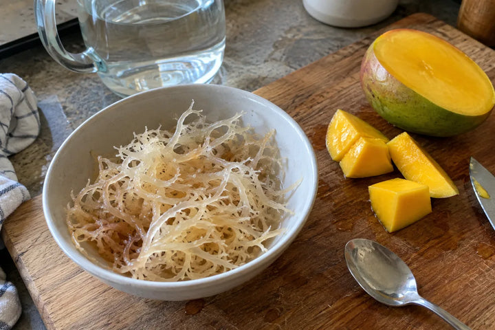 Hydrated sea moss in a bowl beside water and freshly cut mango