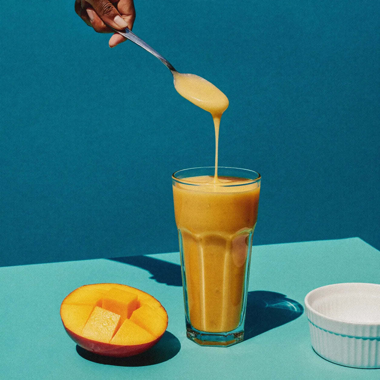 A hand stirring a smoothie beside a breakfast bowl; serving suggestion